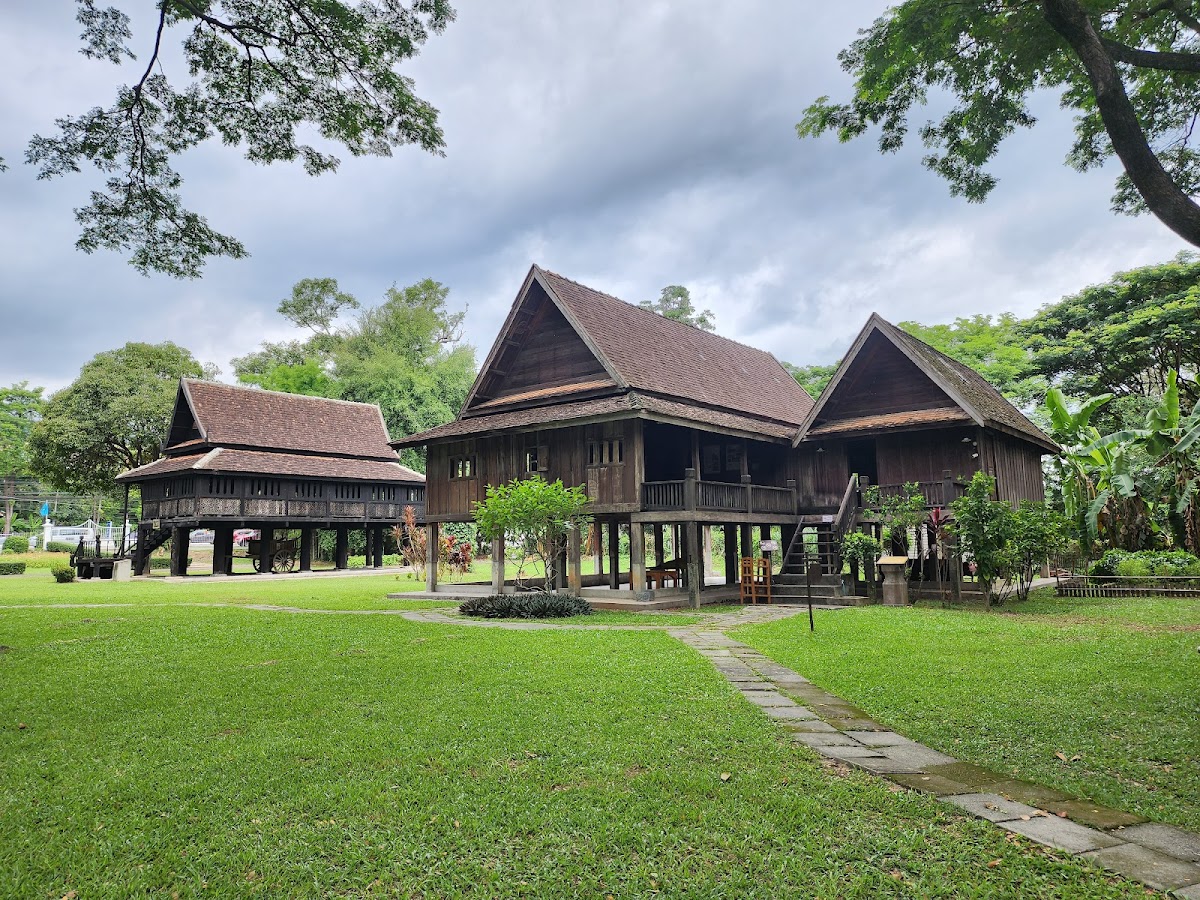 Traditional Lanna stilt houses with steep peaked roofs surrounded by green lawn at the Lanna Traditional House Museum