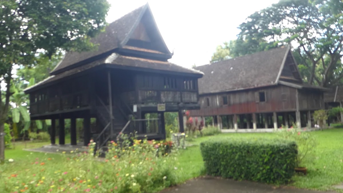 Dark teak Lanna houses on stilts with flower garden in the foreground